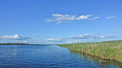 Peaceful landscape of Africa. Sunny summer day. The blue river flows calmly, green grass grows on the shore. Azure sky with picturesque clouds. Botswana, Chobe.