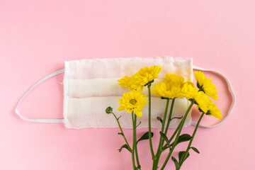 Seasonal spring summer allergy flowers concept. Yellow flowers with medical protective mask on pink background. Creative flat lay composition, copy space