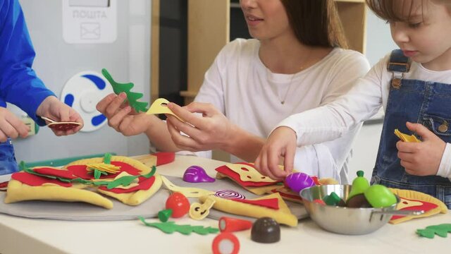 Caucasian girl and boy kid playing and learning at preschool with female teacher. Mother, daughter adn son playing cooking