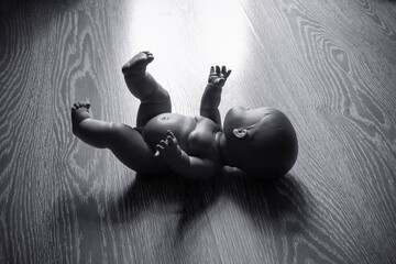 Baby doll on a wooden floor, symbol of abortion, dead child, miscarriage. Black and white dramatic...