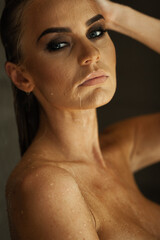Relaxation and spa concept. Portrait of a sexy fashionable lady in a black swimsuit. Woman with wet hair and makeup poses in shower near swimming pool in natural light