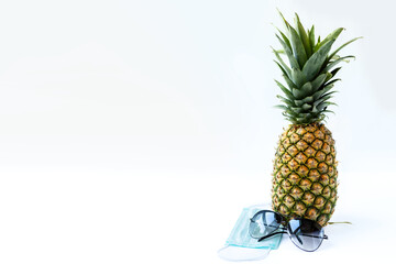 Pineapple, sunglasses and medical mask on a white background. Summer concept 2020 during the coronavirus pandemic.