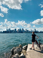 Young woman with bicycle enjoying cityscape view on Toronto city in Canada. Sport summer activity in modern large town. Canadian Toronto islands landmark. Sunny day nature in Ontario.