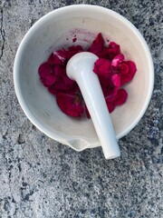 
White mortar and pestle filled with bright red roses on a grey background