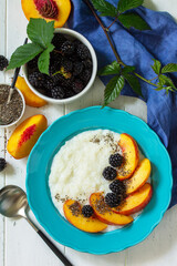 Healthy food for Breakfast, diet food concept. Rice porridge with chia, peach and blackberry in a bowl on a white wooden table. Top view flat lay background. Copy space.