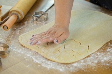 woman's hand slices sheet of dough with cookie mold in shape of heart and flowers for homemade...