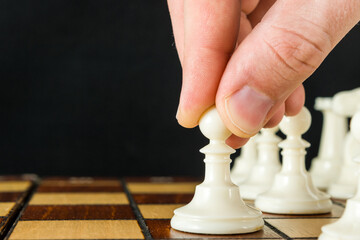 Part of a man's hand making the first move in a chess game, moving a pawn one square forward. Black background.