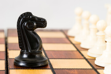 Chess piece of a black horse in the middle of the playing Board against a row of white pieces,...