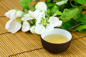 Plakat Green tea in a ceramic cup with branches of blossoming cherry tree on a bamboo background. Spring background.