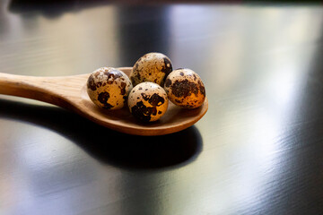 Quail eggs with speckles in a wooden spoon on a dark shiny table. Healthy eating, bird eggs. Cooking breakfast, ingredient, cuisine. Group of objects, close-up.