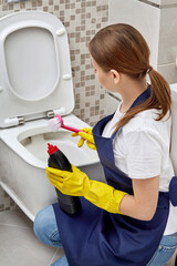 Brunette girl washes the toilet in gloves for cleaning. Professional cleaning.