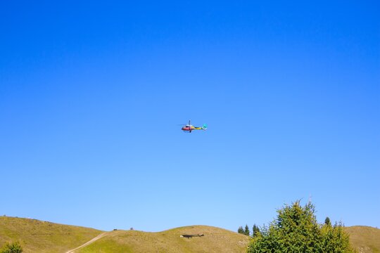 Helicopter Eurocopter EC 130 B4 in blue sky over green hills.