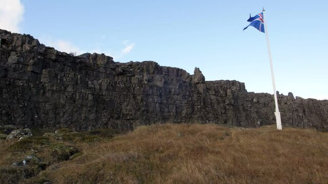 Flag of Iceland in slow motion winds against volcanic cliff at Logberg.