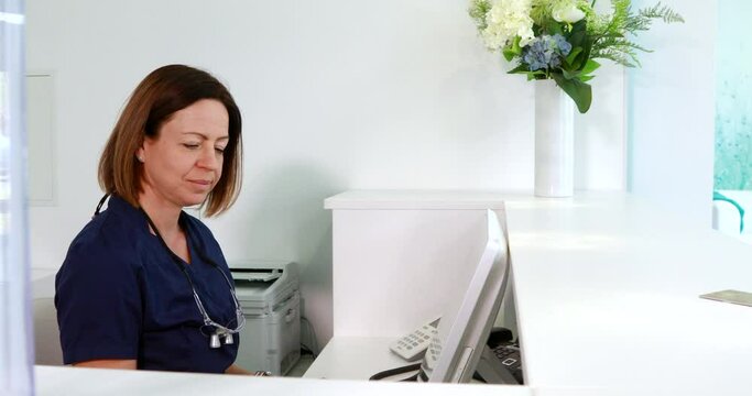 Doctor's assistant at front desk on the phone, dentist passing by