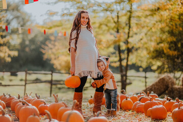 Young pregnant woman in white autumn cardigan posing with a little son in fox coat at the pumpkin's...