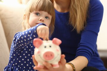 Child little girl arm putting pin money coins into happy pink faced piglet slot portrait. Making effective future needs savings collect dollar gift benefit present home leisure concept