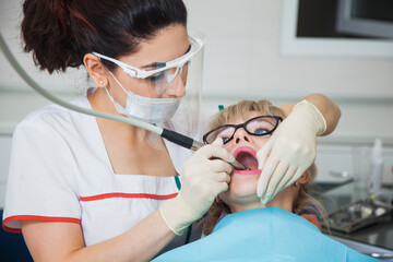 Closeup shot of dentist in protection mask working with tooth cavity and plague. Patient on...