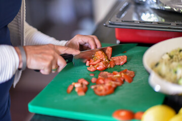 Woman is cutting tomatoes to little pieces in the kitchen for a homemade vegetarian salad
