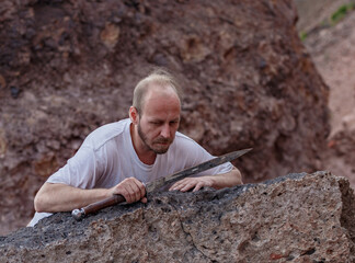 Warlike wanderer in the mountains resting after a battle with a dagger in his hand