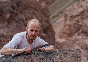 Warlike wanderer in the mountains resting after a battle with a dagger in his hand