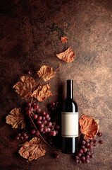 Bottle of red wine with ripe grapes and dried up vine leaves. Old copper background.