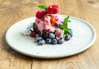 Vegan chocolate brownie topped with fresh organic berries. A sweet chocolate dessert on a ceramic plate.
