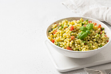 Vegetable salad with pasta ptitim on white table. Close up. Copy space.