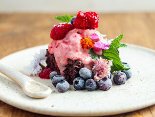 Vegan chocolate brownie topped with fresh organic berries. A sweet chocolate dessert on a ceramic plate.