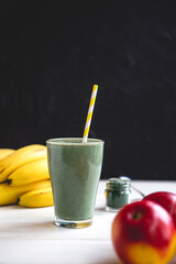 The concept of food and drink, diet and nutrition. Healthy green vegan smoothie with banana, spirulina and ripe apple for summer detoxification