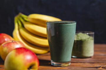 Fresh mixed green fruit smoothie with matcha powder in a glass cup with a straw. Solid background, copy space