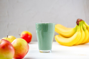 The concept of food and drink, diet and nutrition. Healthy green vegan smoothie with banana, spirulina and ripe apple for summer detoxification