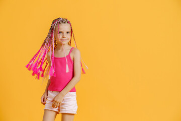 Stylish girl with pink dreadlocks posing in bright clothes on a yellow background. Beauty, fashion.