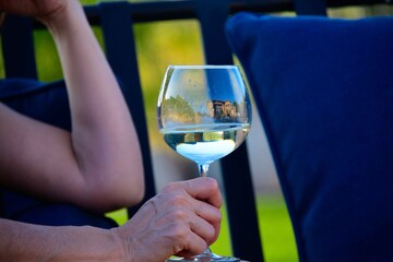 A person holding a wine glass on an outdoor couch with a blue cushion.