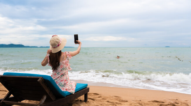 Traveler Asian girl taking selfie with phone on the beach chair.
