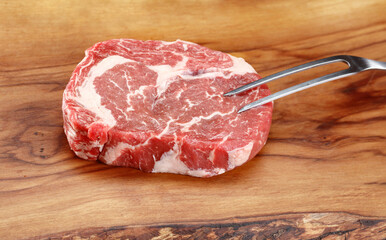Raw fresh Ribeye Steak on a wooden board with meat fork 