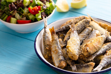 Fried sardines with lemon and salad on wooden background