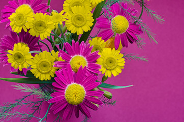 A bouquet of bright yellow and purple summer flowers is shot close-up from the top point on a purple background
