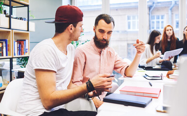 Business couch checking students task watching video about advertising via smartphone using wireless connection. Male colleagues concentrate on solving problems with digital device sitting in office