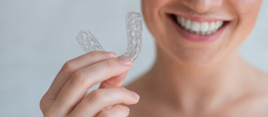 Close-up of orthodontic silicone transparent teeth aligner in female hands. Unrecognizable woman holding a removable night retainer. Bracket for teeth whitening. The perfect smile. Cropped photo.