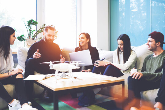 Young Crew Of Male And Female IT Professionals Discussing Idea Of Creation Application For Drone And Other Digital Devices Using Modern Laptop Computer And Wireless Connection To Internet In Office