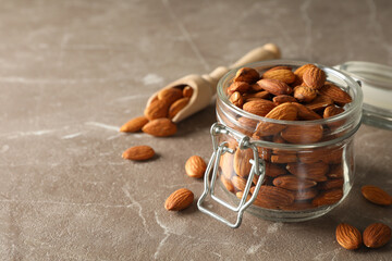 Wooden scoop and glass jar with almond on gray table. Vitamin food