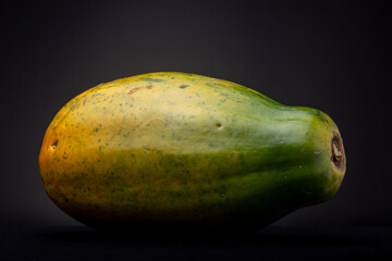 Colourful large orange, yellow and green fresh tropical red papaya fruit against a dark background. Studio low key food still life.
