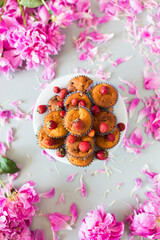 Obraz na płótnie Canvas Homemade cupcakes with strawberry inside and outside on white plate surrounded with the petals of peonies
