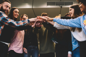 Cheerful skilled dream team members in casual outfit laughing while standing in coworking space.Multicultural group of IT programmers in good mood emotionally celebrating completed startup project