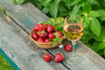 Glass of rose wine served with fresh strawberries on wooden background. Picnic outdoor with pink wine and berries.