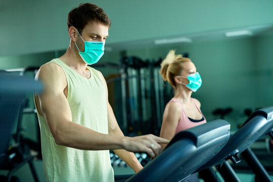 Athletic couple with protective face mask exercising on treadmill at the gym.