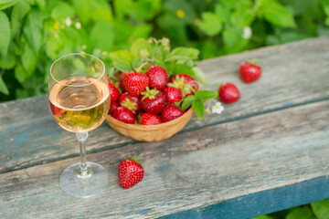 Glass of rose wine served with fresh strawberries on wooden background. Picnic outdoor with pink wine and berries.