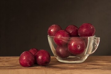 Glass bowl with red plums on a wooden table and copy space