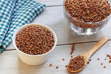 Bowl of raw buckwheat with spoon on wooden background