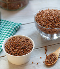 Bowl of raw buckwheat with spoon on wooden background